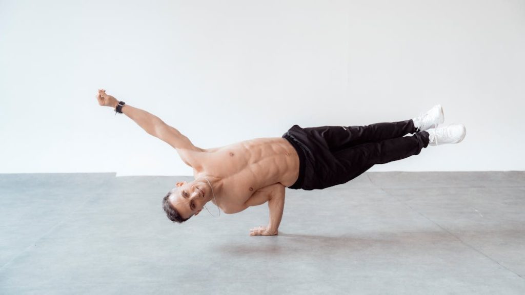 A shirtless male breakdancer in a one-handed freeze pose on a studio floor.
