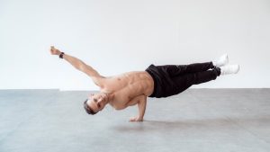 A shirtless male breakdancer in a one-handed freeze pose on a studio floor.
